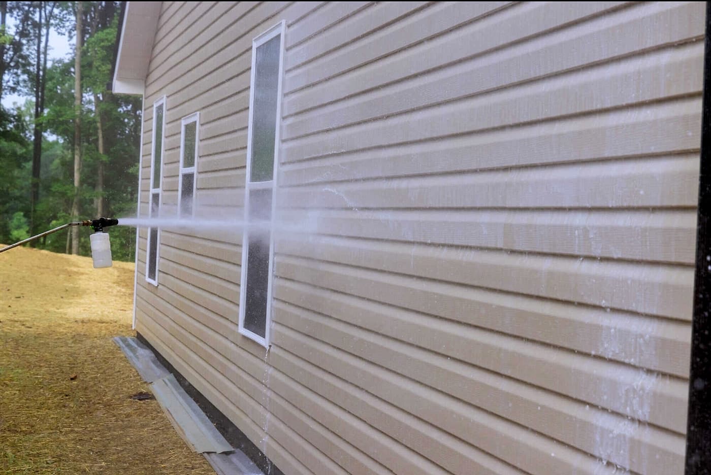 Pressure washer spraying and rinsing vinyl siding on a house